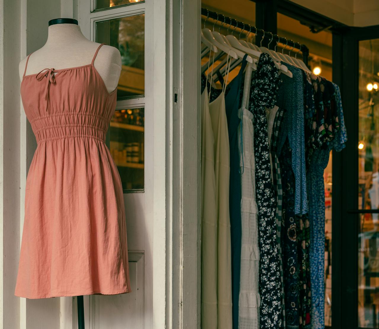 about-us Mannequin with a pink dress and clothing rack in a stylish boutique.