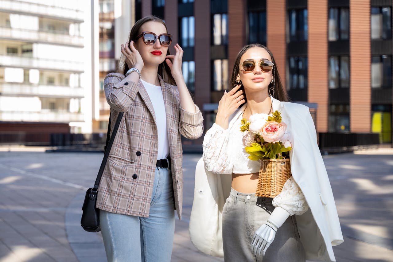 about-us Two stylish women enjoy a sunny day in the city wearing chic outfits and sunglasses.